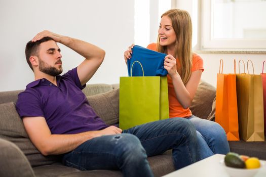 Couple having conflict because wife spent too much money on shopping while they sitting at sofa in their home.
