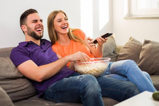 Happy couple enjoy watching tv, eating popcorn and spending time together at their home.