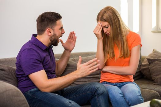 Angry wife and husband are having conflict while they sitting on sofa at their home.