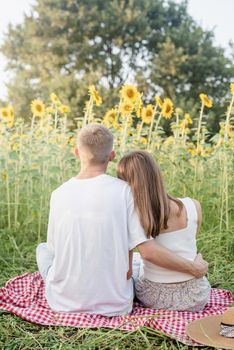 Autumn nature. Fun and liesure. Young teenage couple picnic on sunflower field in sunset, enjoying time together, rear view