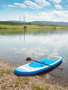 Blue paddleboard is waiting stretched out on a sandy beach of Milada lake