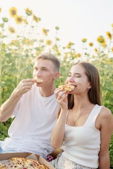 Autumn nature. Fun and liesure. Young teenage couple picnic on sunflower field in sunset eating pizza