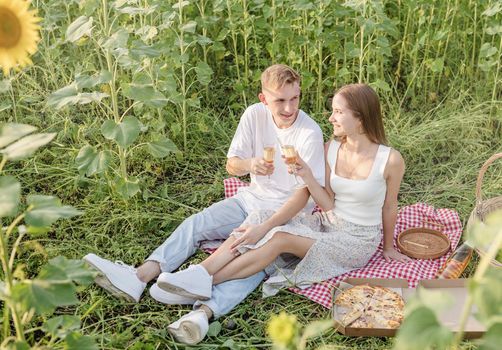 Autumn nature. Fun and liesure. Young teenage couple picnic on sunflower field in sunset drinking champagne