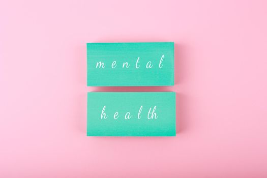 Creative flat lay with blue blocks with written mental health text on bright pastel pink background. Concept of world mental health day, mental health assessment and awareness