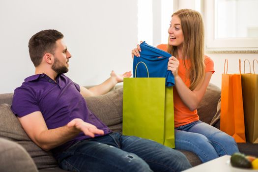 Couple having conflict because wife spent too much money on shopping while they sitting at sofa in their home.