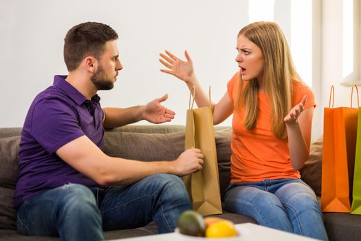 Couple having conflict because wife spent too much money on shopping while they sitting at sofa in their home.