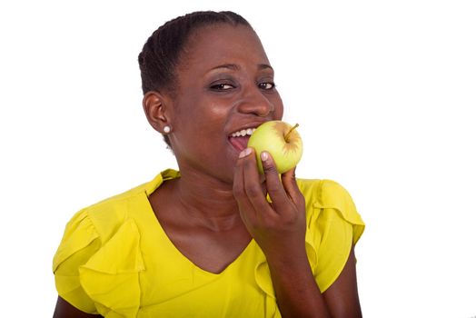 young girl standing in yellow camisole holding an apple on her mouth and looking at camera smiling.
