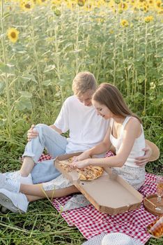 Autumn nature. Fun and liesure. Young teenage couple picnic on sunflower field in sunset drinking champagne