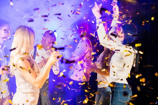 People dance at party in nightclub, drink champagne in falling confetti