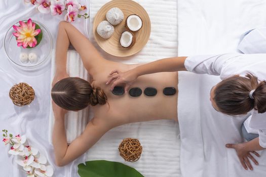 Spa stone massage, beautiful woman getting hot stones massage, beauty treatments concept. Top view. Orchid and lotus flowers coconut and herb pouches