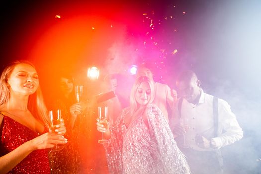 People dance at party in nightclub, drink champagne in falling confetti