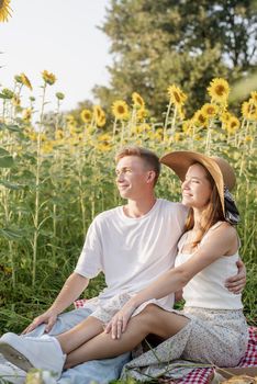 Autumn nature. Fun and liesure. Young teenage couple having picnic on sunflower field in sunset, having fun looking away