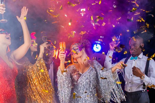 People dance at party in nightclub, drink champagne in falling confetti