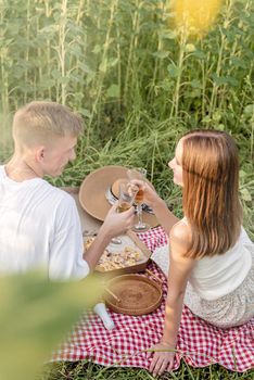 Autumn nature. Fun and liesure. Young teenage couple picnic on sunflower field in sunset drinking champagne toasting