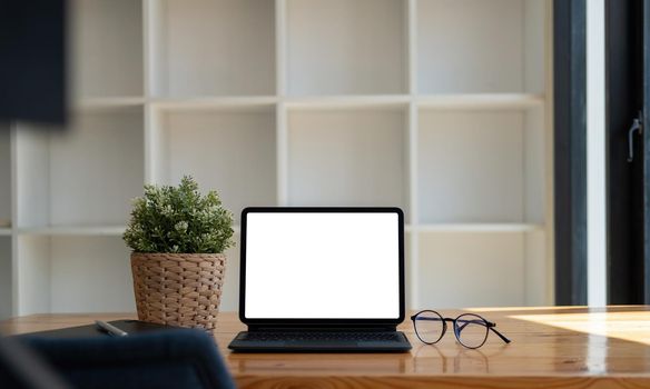 Mock up of blank screen tablet with keyboard on wooden desk at home office.