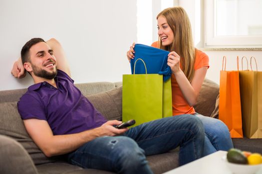 Wife is showing to her husband her new t-shirt,but husband is not interested and watching tv.