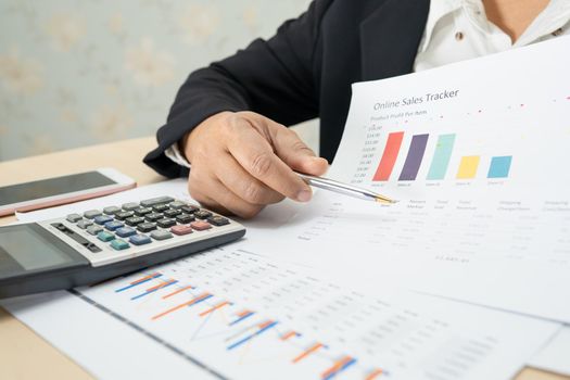 Asian accountant working and analyzing financial reports project accounting with chart graph and calculator in modern office, finance and business concept.