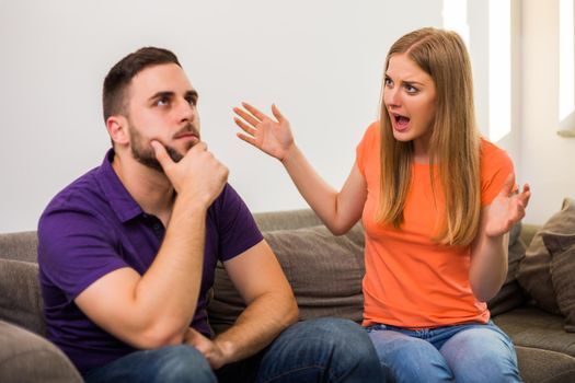 Angry wife and husband are having conflict while they sitting on sofa at their home.