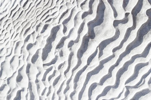 White and gray texture background of Pamukkale calcium travertine in Turkey, pattern of diagonal waves, close-up.