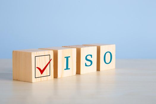 The abbreviation ISO on wooden cubes with check mark on blue background. ISO quality control certification approval concept.