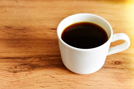 White cup of strong black coffee on wooden surface close up.