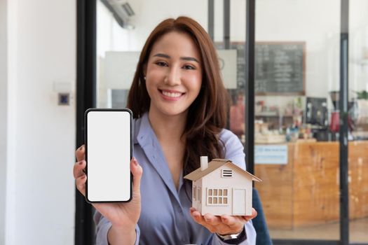 Real estate agent showing house model and mobile phone with blank white screen for advertisement.