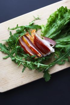 Sliced ham with fresh green lettuce and ruccola leaves on a cutting board.