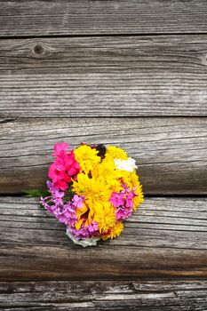 Bouquet of bright summer flowers on rough weathered wooden wall background.