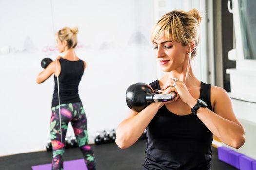 Beautiful woman is practicing kettlebell pilates in gym.
