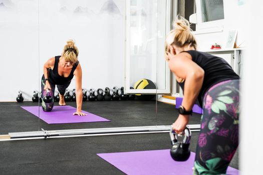 Beautiful woman is practicing kettlebell pilates in gym.