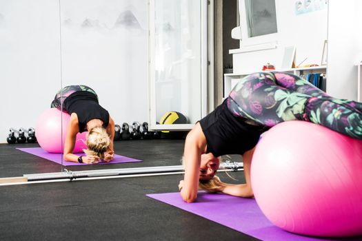 Adult woman is practicing pilates with fitness ball in gym.