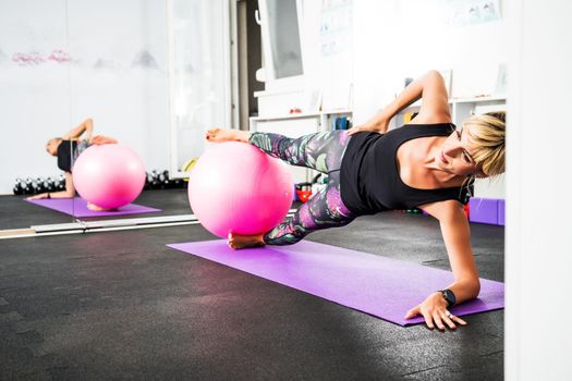 Adult woman is practicing pilates with fitness ball in gym.
