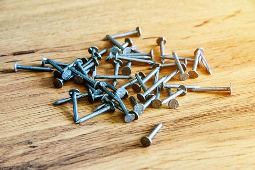 Heap of thin metal nails close up on wooden surface.