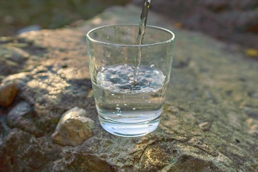 Water pour into glass on summer scene background