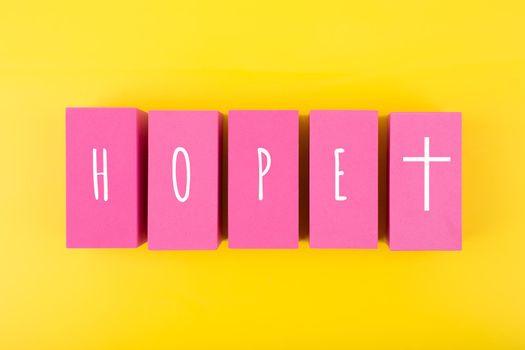 Modern religious minimal concept of hope with christian cross on bright yellow background. Biblical creative composition with single word hope and cross