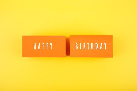 Happy Birthday bright fun colorful concept on yellow background. Happy Birthday written on orange tablets against yellow background