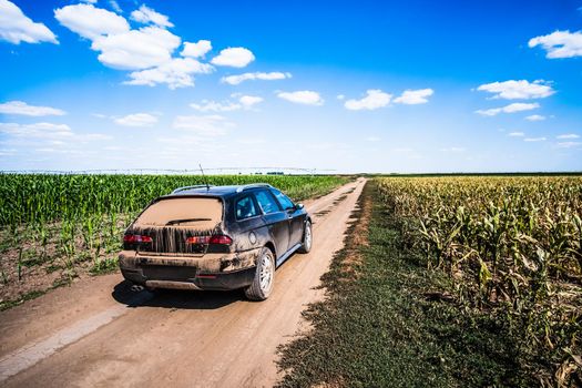 Sports utility vehicle on a dusty road in countryside in summer.