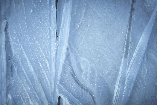 The surface of natural ice covering the puddle in late autumn. Ice texture with intersperses of white frost, crystals of frozen water. Rime.