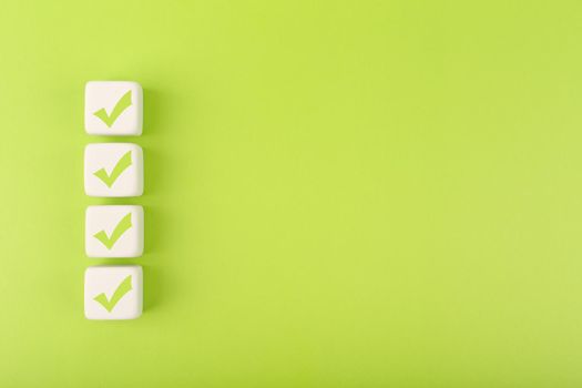 Four checkmarks on white cubes against bright green background with copy space. Concept of questionary, checklist, to do list, planning, business or verification. Creative minimal composition 