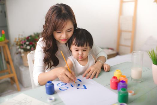 Happy family mother and daughter together paint. Asian woman helps her child girl.