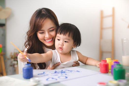 Happy family mother and daughter together paint. Asian woman helps her child girl.