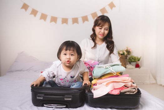 Asian mom and baby girl with suitcase baggage and clothes ready for traveling on vacation