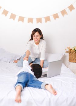 Young asian mom working while her baby girl sitting on floor at home.