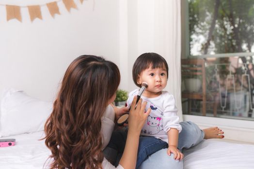 Lovely princess is applying the make up on her skin with special brush as she wants to look like her adult mother