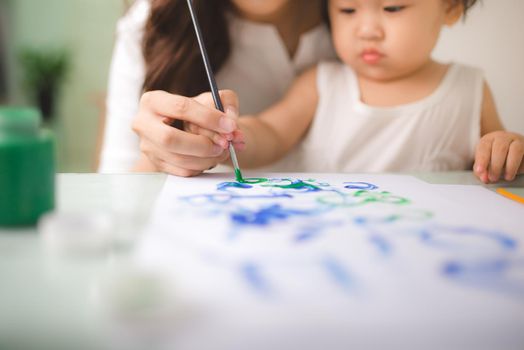 Happy family mother and daughter together paint. Asian woman helps her child girl.