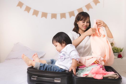 Asian mom and baby girl with suitcase baggage and clothes ready for traveling on vacation