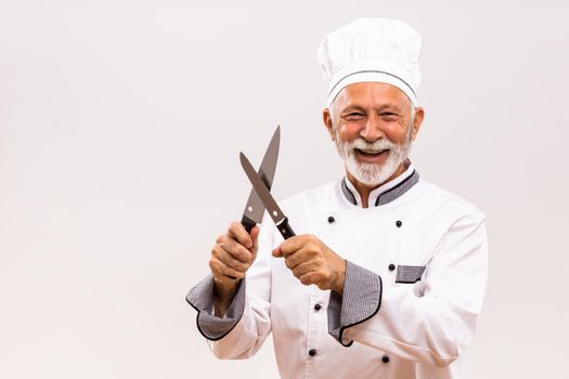Image of happy chef sharpens knives on gray background.