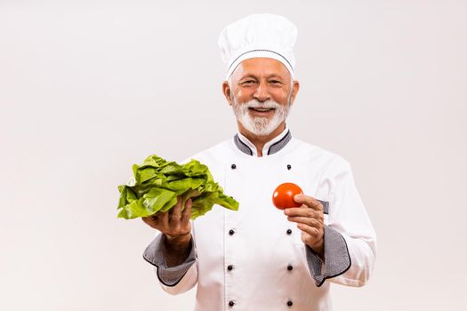 Portrait of senior chef holding vegetables on gray background.