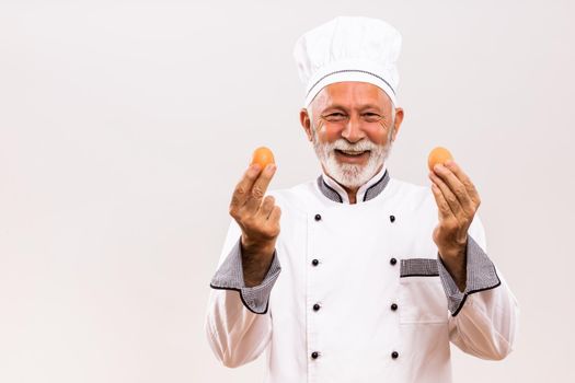 Image of  senior chef holding eggs on gray background.