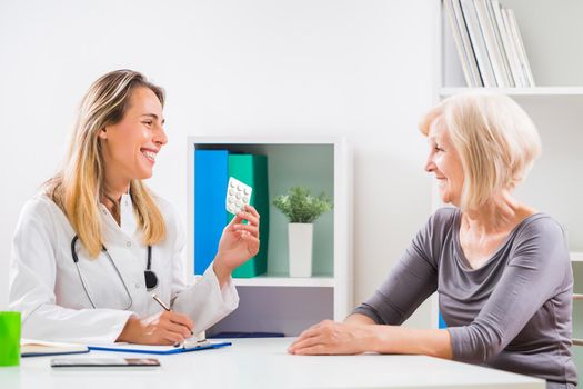 Female doctor is writing prescription to her senior patient for her health problems.